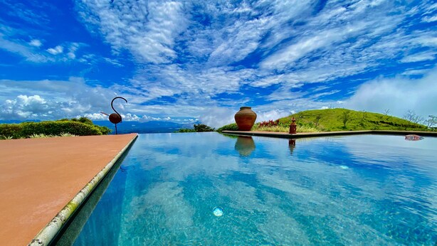 Un cielo azul despejado con nubes, una piscina y un jarrón grande en el borde.