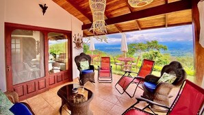 Un patio amplio con mobiliario de mimbre, un vidrio que da a un comedor y vistas al paisaje.