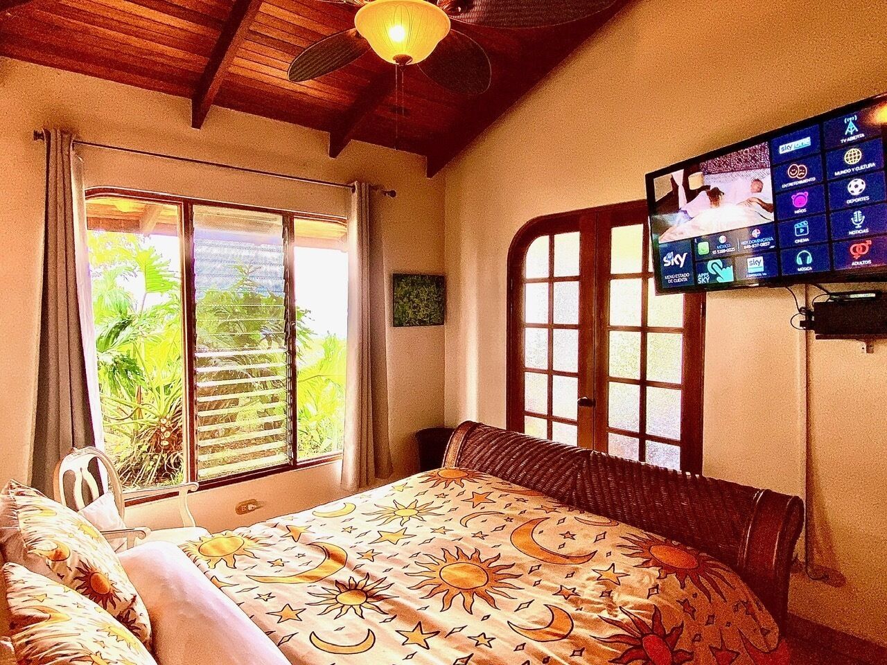 Quarto com cama, televisão na parede e janela com persianas.
