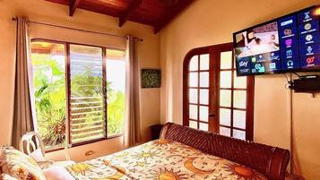 Quarto com cama, televisão na parede e janela com persianas.