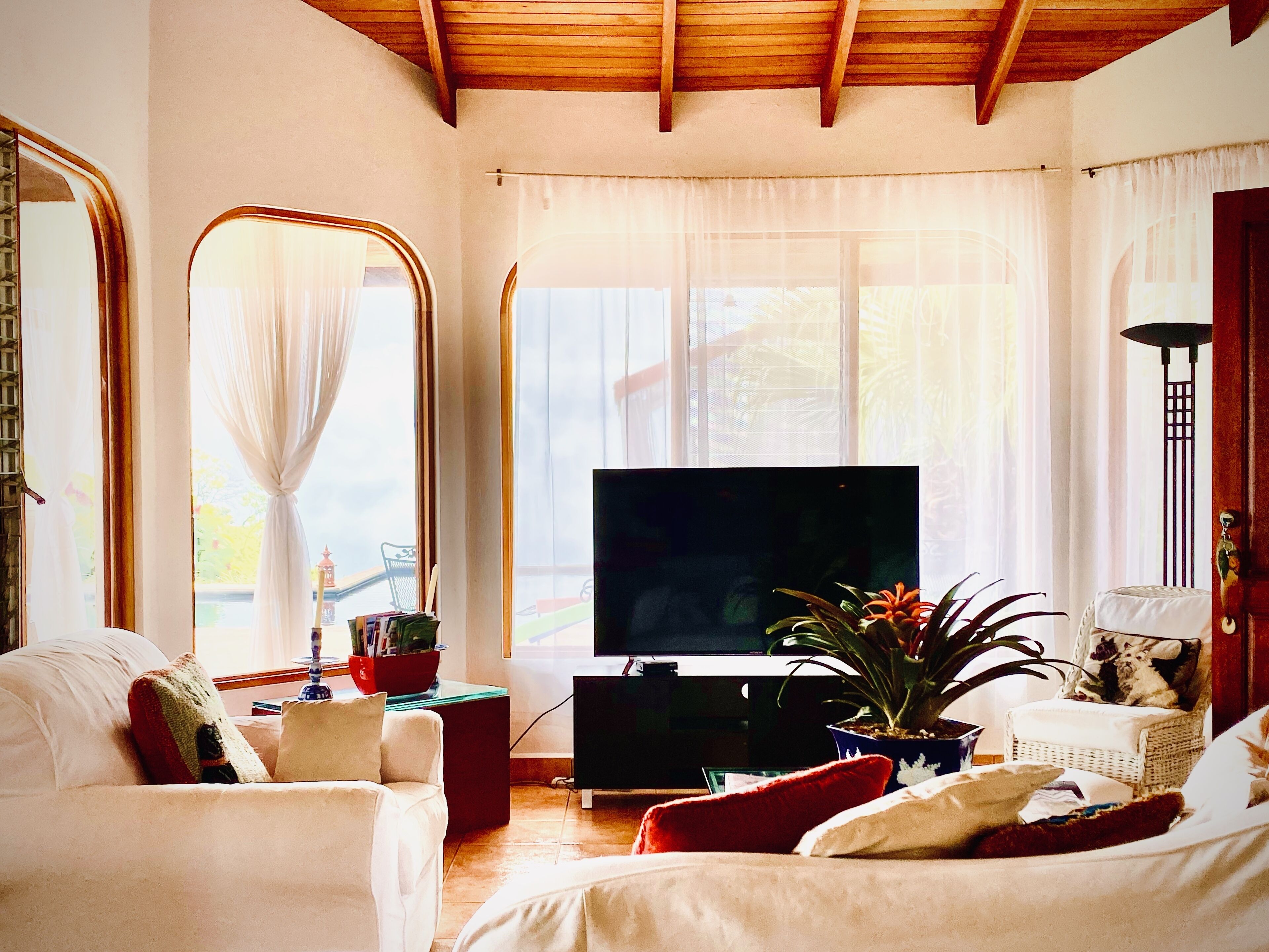 Een woonkamer met een televisie, een bank, een stoel, een grote spiegel en een raam met gordijnen.