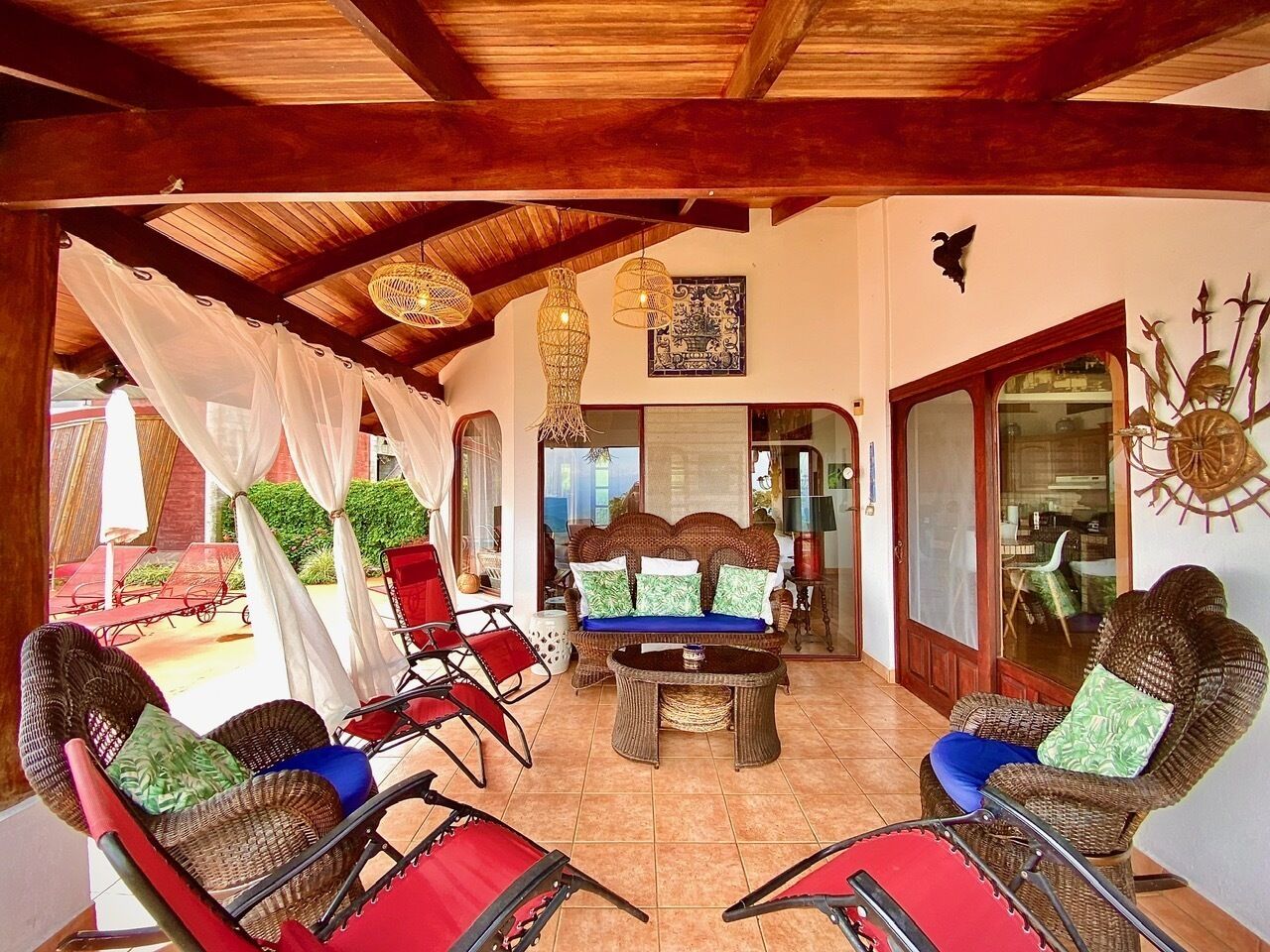 Un espace extérieur aménagé, abrité et doté de mobilier en osier et d’un canapé, avec un plafond en bois et une vue sur l’extérieur.