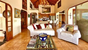 Un amplio espacio de estar con techo de madera alto, un comedor y una cocina al fondo, y un ventanal con vistas.