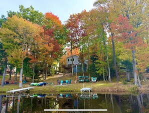 A lakeside property with a dock, outdoor seating, and a house surrounded by autumn-colored trees.