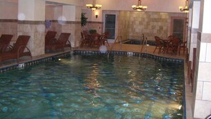 Una piscina interior con agua cristalina, rodeada de sillas y mesas de madera, y paredes de piedra.