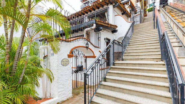 A staircase with a white wall and metal railings, leading to a building with a tiled roof and balconies. - Condo in Olas Altas 1  1BD Studio for rent in Old Town, Puerto vallarta (Puerto Vallarta)