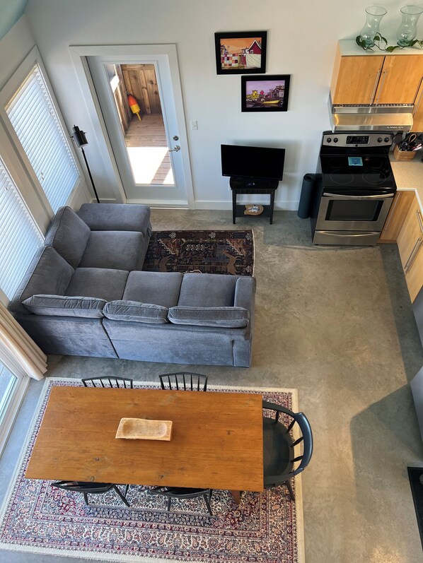 Un espacio habitable moderno con un sofá seccional gris, una mesa de comedor de madera y una cocina con estufa y horno.