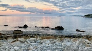 Un rivage rocheux bordé d’une eau calme, avec une étendue de terre visible au loin, sous un ciel nuageux.