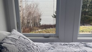 Une chambre avec une grande fenêtre, un lit recouvert d’une couvre-lit à motifs, et une vue sur des arbres et une étendue d’eau à l’extérieur.