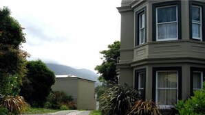 A two-story building with a bay window on the second floor, surrounded by lush greenery and a clear sky. - Toogooloowa on Davey 3 (Hobart)