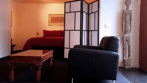 A room with a bed, a black chair, a wooden table, and a decorative wooden sculpture. - Toogooloowa on Davey 3 (Hobart)