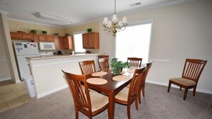 Un comedor con una mesa y sillas de madera, una araña y una cocina al fondo.