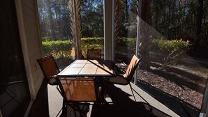 Un porche cubierto con una mesa y sillas, con vistas a una zona boscosa.