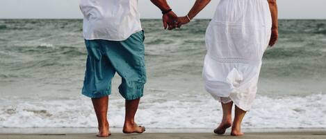 Two people holding hands on a beach with waves in the background.