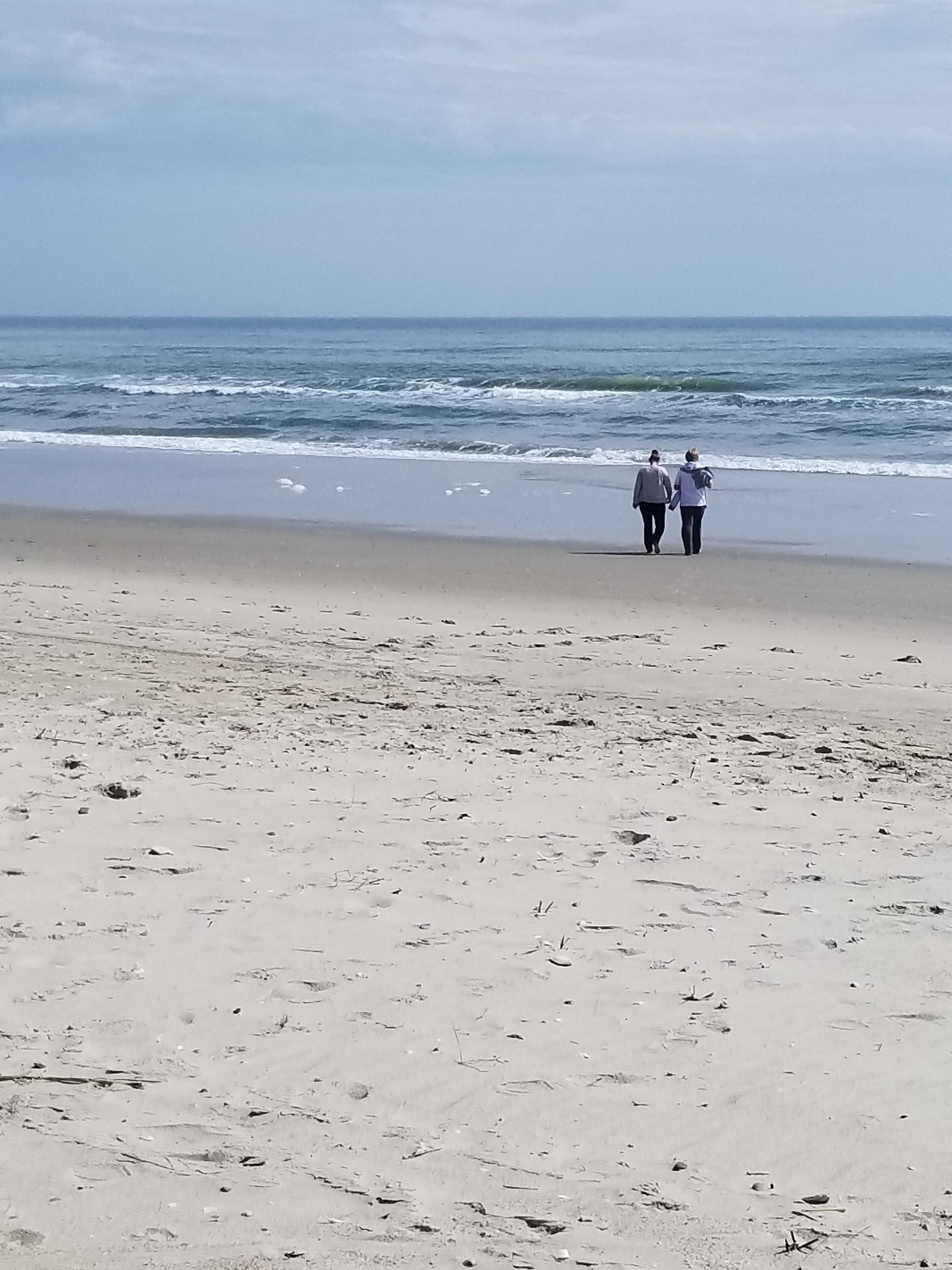 A beach with two people walking along the shore.