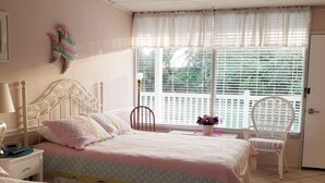 Ein Schlafzimmer mit zwei Betten, einem Fenster mit Jalousien, einem Sessel und einem kleinen Tisch.