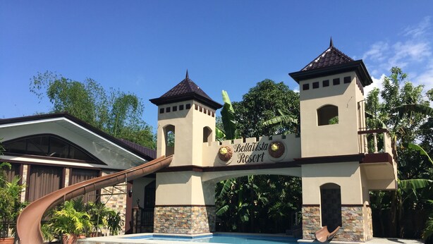 Entrada de un resort con piscina, destacándose un letrero con figuras de leones y el nombre 'BellaVista Resort'.