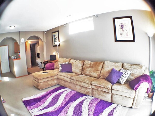 A living room with a sectional sofa, a purple and white striped rug, and a framed picture on the wall.