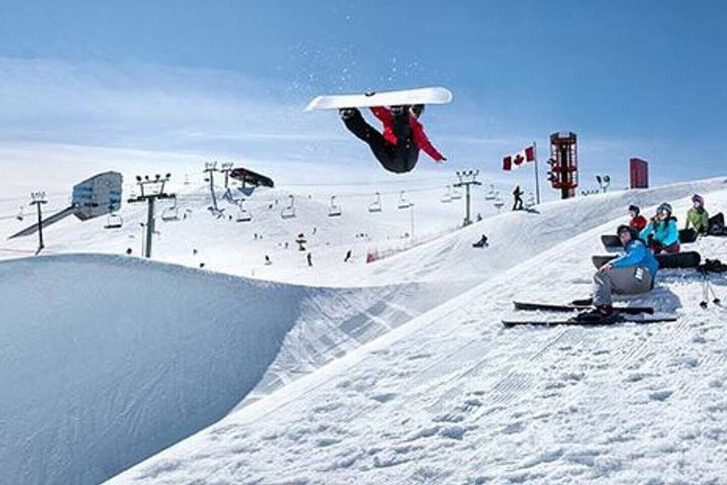Um snowboarder executando uma manobra em uma encosta nevada, com um teleférico ao fundo.