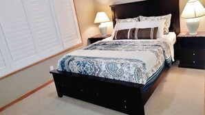 A bedroom with a dark wood bed, patterned bedding, two bedside lamps, and a large window with blinds. - Bright, Welcoming Mountain Escape! Near Downtown! (Calgary)