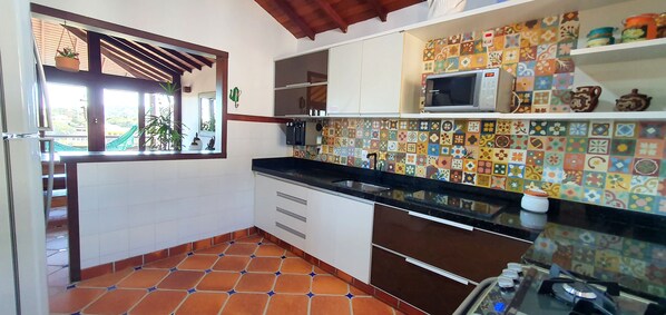 A kitchen with a tiled backsplash, a microwave, and a window with a view of a green landscape. - EXCELLENT HOUSE IN GERIBÁ, 500m FROM THE BEACH! BEAUTIFUL VIEW. 4 BEDROOMS, AIRY, COZY (Armação dos Búzios)