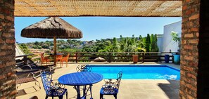 A pool area with a thatched umbrella, metal chairs, and a view of a hillside with houses. - EXCELLENT HOUSE IN GERIBÁ, 500m FROM THE BEACH! BEAUTIFUL VIEW. 4 BEDROOMS, AIRY, COZY (Armação dos Búzios)