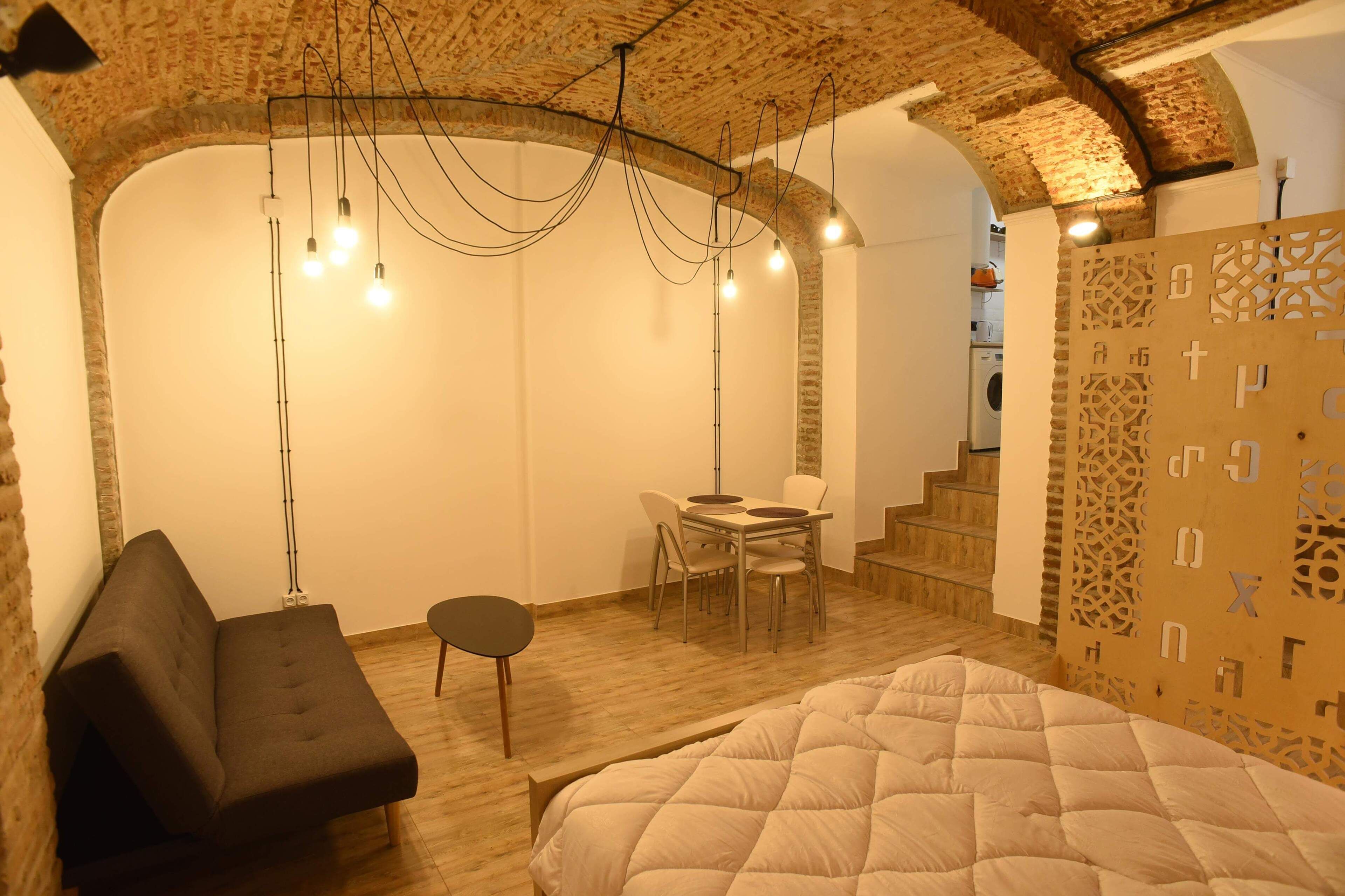 Una habitación acogedora con una cama, un sofá, una mesa de comedor y una escalera.