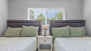 Ein Schlafzimmer mit zwei Betten, einem Nachttisch mit Lampe und einem Fenster mit Jalousien.