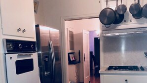 Une cuisine avec des armoires blanches, un comptoir noir et une cuisinière. Un réfrigérateur et un four à micro-ondes se trouvent à gauche. Des casseroles sont suspendues au-dessus de la cuisinière.