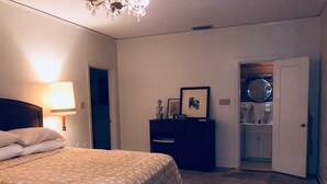 Une chambre à coucher comprenant un lit, une commode, un miroir et une porte donnant sur une salle de bain.