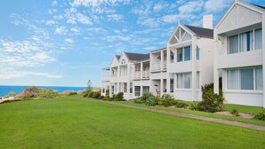 A row of white two-story houses with balconies, a well-maintained lawn, and a view of the ocean. - Quarterdeck 4 @ Lennox Head (LENNOX HEAD)