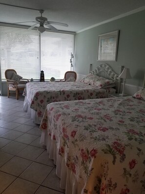Un dormitorio con dos camas, una silla, una mesa y un ventilador de techo.
