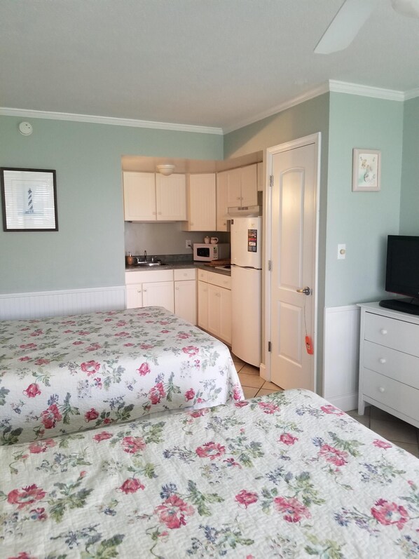Un dormitorio con dos camas, una kitchenette pequeña, un televisor y un cuadro en la pared.