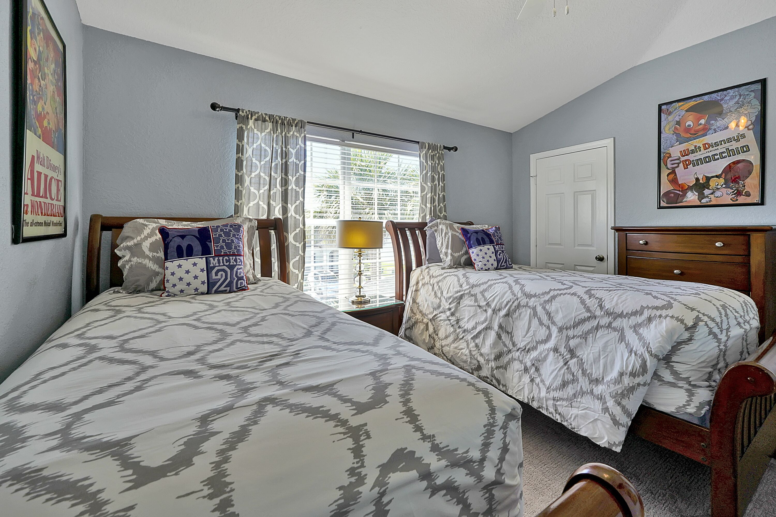 A bedroom with two beds, a window with curtains, a lamp, and a poster on the wall.