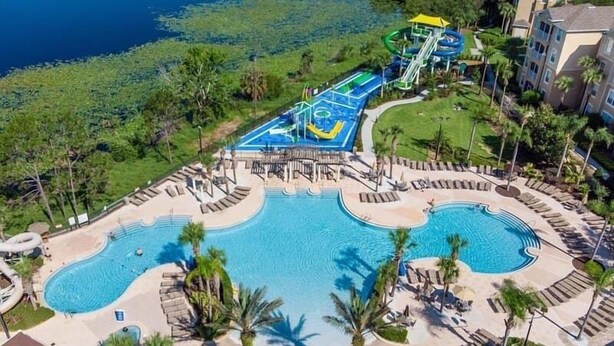 A resort with a large pool, water slides, and lounge areas surrounded by palm trees. - Lake View End Unit Town Home Closest to ALL of the Amenities at WINDSOR HILLS (Kissimmee)