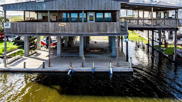 A two-story waterfront building with a dock, a sign for rent, and a view of the water.