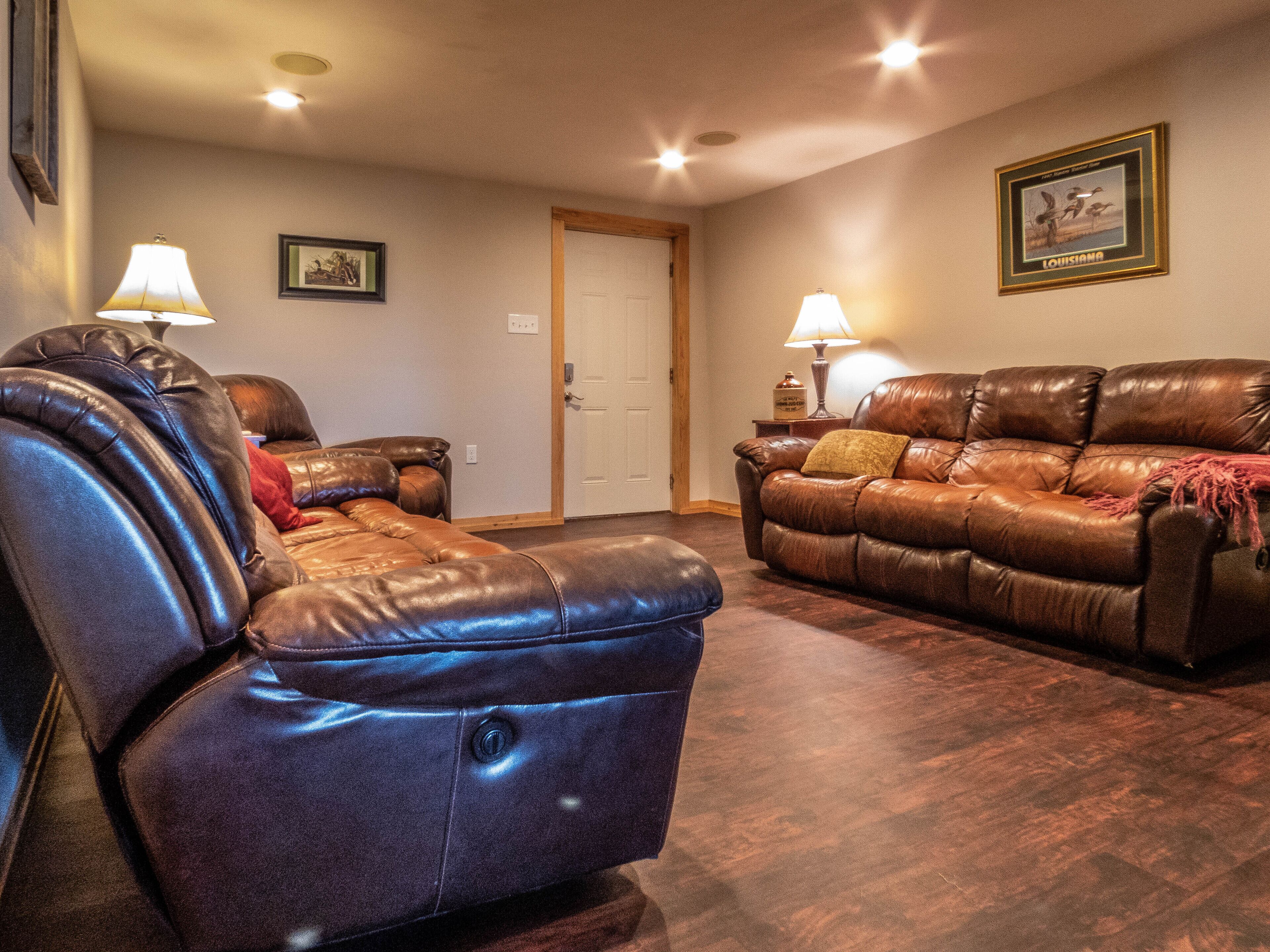 A living room with two leather sofas and a recliner, a door, and a framed picture on the wall.