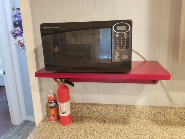A microwave on a red shelf with a fire extinguisher and a can of fire extinguisher underneath. - Reel'em Inn - Adventures Start Here! (Port O'Connor)