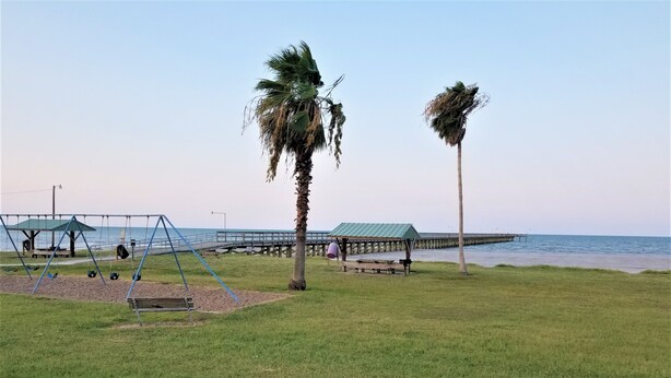 A beach park with swings, a picnic area, and a pier extending into the water. -  Reel'em Inn - Adventures Start Here! (Port O'Connor)