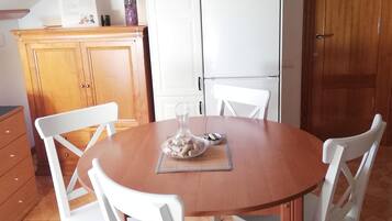 Een eetruimte met een ronde houten tafel, omringd door witte stoelen, een witte koelkast en houten kasten.