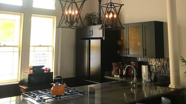 A modern kitchen with a central island, pendant lights, and a view of the outdoors. - The Bell Tower Loft at Sanctuary Place (Savannah)