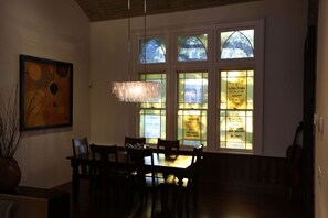 A dining area with a table and chairs, a chandelier, and a stained glass window with text. - The Bell Tower Loft at Sanctuary Place (Savannah)