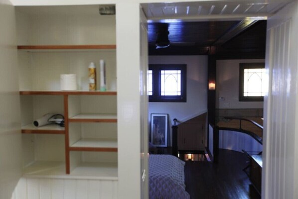 A room with a bed, a wooden shelf unit, and a staircase leading to an upper level. - The Bell Tower Loft at Sanctuary Place (Savannah)