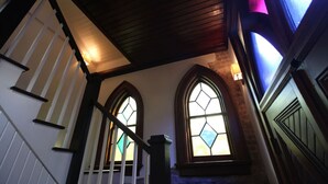 A staircase with a wooden handrail, a white wall, and a stained glass window. - The Bell Tower Loft at Sanctuary Place (Savannah)