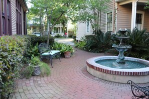 A brick pathway leading to a fountain surrounded by lush greenery and a bench. - The Bell Tower Loft at Sanctuary Place (Savannah)