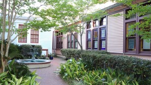 A courtyard with a fountain, a pathway, and a building with large windows and a brick facade. - The Bell Tower Loft at Sanctuary Place (Savannah)