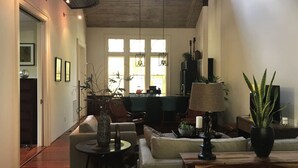 A spacious living room with a high ceiling, a dining area, and a kitchen visible through the windows. - The Bell Tower Loft at Sanctuary Place (Savannah)