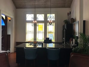 A kitchen with a central island, two hanging pendant lights, and a view through large windows. - The Bell Tower Loft at Sanctuary Place (Savannah)