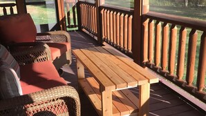 A covered outdoor seating area with wicker furniture and a wooden table, overlooking a forested landscape. - Log Cabin/screened porch, 9 Acres/ Mountain views (Woodstock)