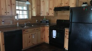 A kitchen with wooden cabinets, a black refrigerator, a stove, and a microwave. - Log Cabin/screened porch, 9 Acres/ Mountain views (Woodstock)
